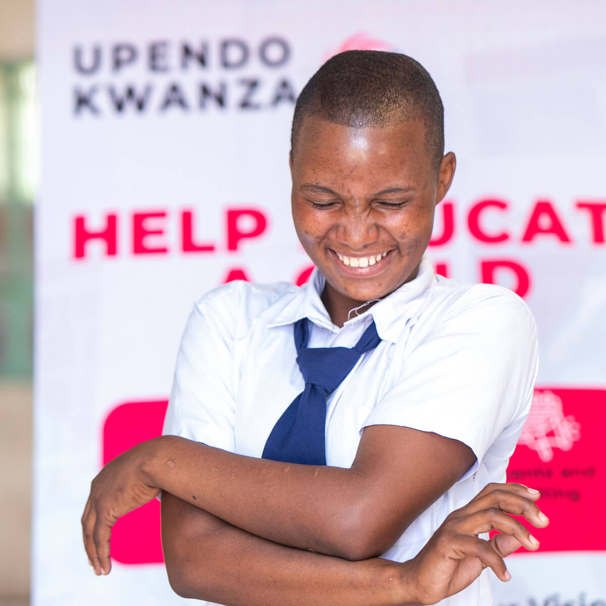 A student smiling bashfully in front of Upendo Kwanza banner