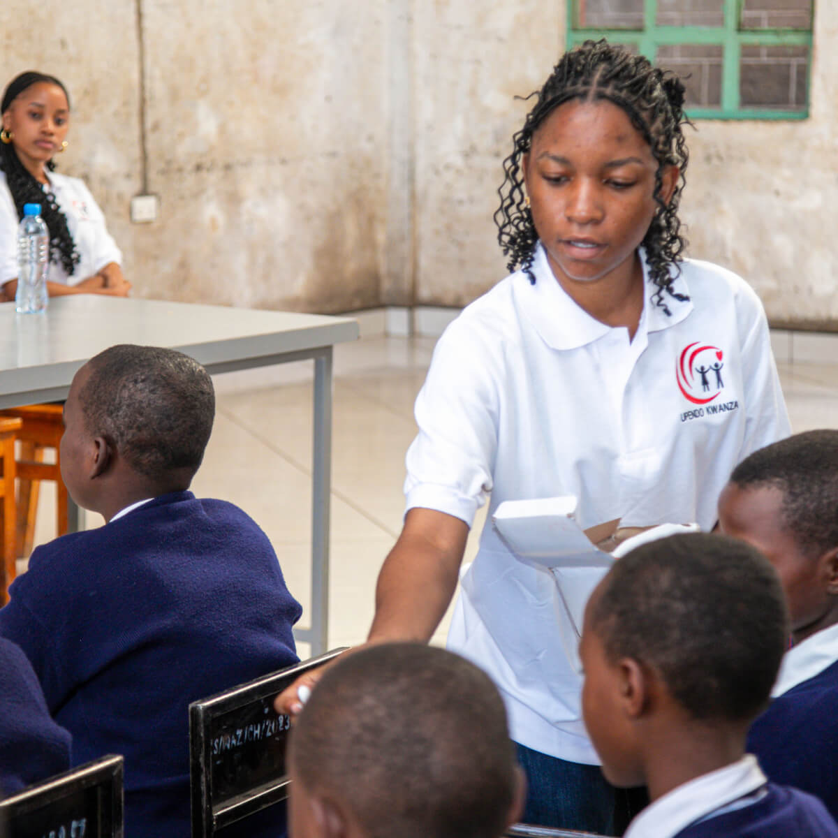 A volunteer hands out school supplies to students in a classroom